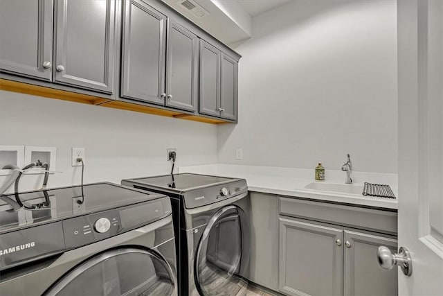 clothes washing area featuring washing machine and clothes dryer, visible vents, cabinet space, and a sink