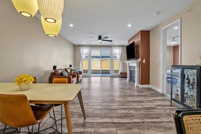 dining area featuring baseboards, recessed lighting, wood finished floors, a glass covered fireplace, and a ceiling fan