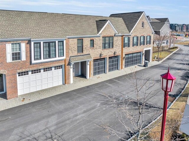 view of front of home featuring a residential view, driveway, brick siding, and an attached garage