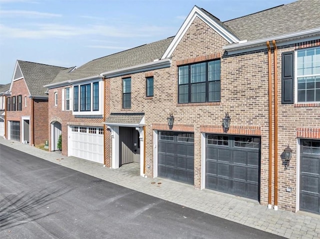 view of property with a garage, brick siding, and a shingled roof