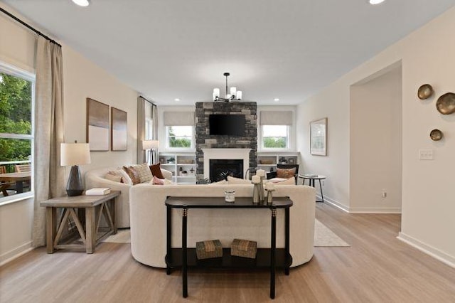 living room with a notable chandelier, recessed lighting, a stone fireplace, light wood finished floors, and baseboards