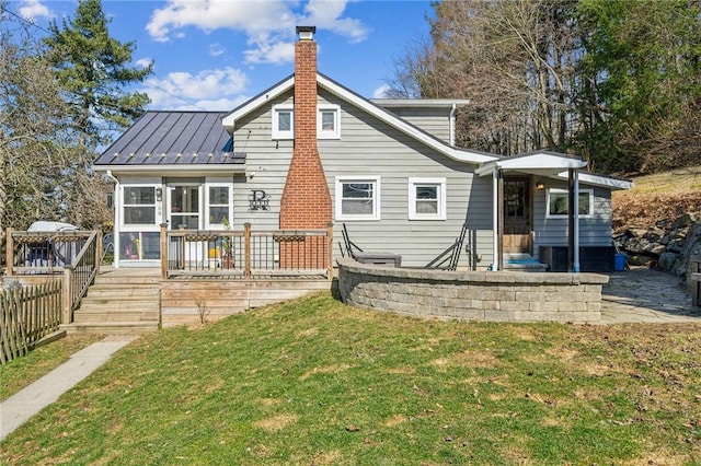 rear view of property with fence, a chimney, metal roof, a yard, and a standing seam roof