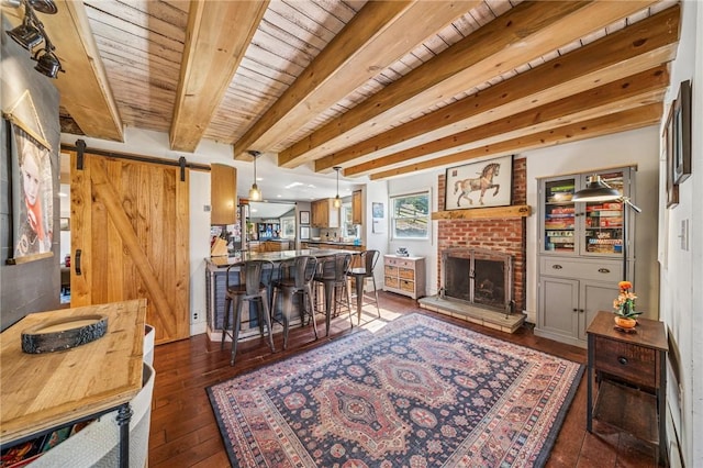 living area with beam ceiling, a fireplace, dark wood-style flooring, a barn door, and wooden ceiling