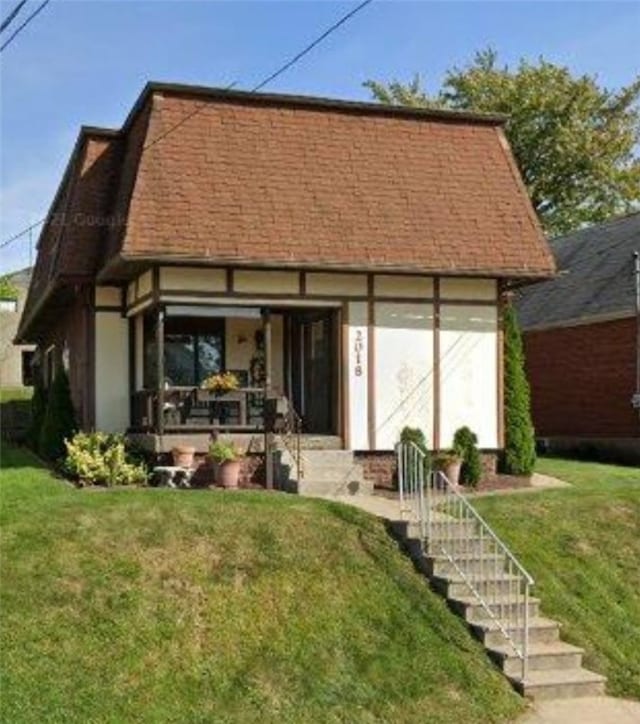 back of property with covered porch, a shingled roof, stairs, and a yard