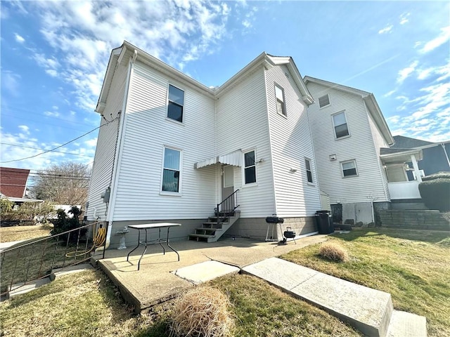 back of property with entry steps, a lawn, and fence