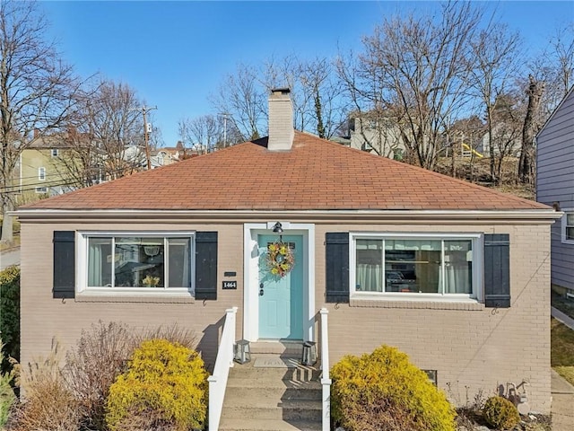 view of front of property featuring crawl space, brick siding, a chimney, and a shingled roof