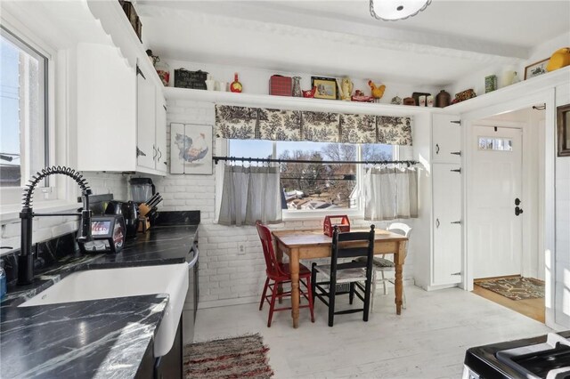 kitchen with a sink, light wood-type flooring, dark countertops, and white cabinets