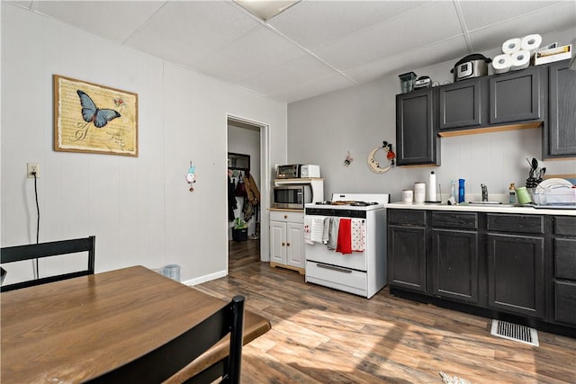 kitchen with wood finished floors, light countertops, a paneled ceiling, stainless steel microwave, and white gas range