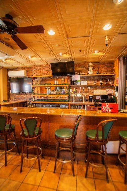 bar featuring a ceiling fan, a wall mounted AC, an ornate ceiling, tile patterned flooring, and a community bar