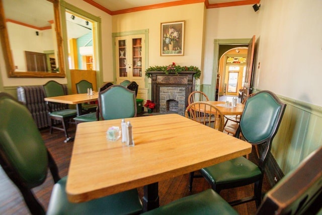 dining space with wood finished floors, a wainscoted wall, a fireplace, arched walkways, and crown molding