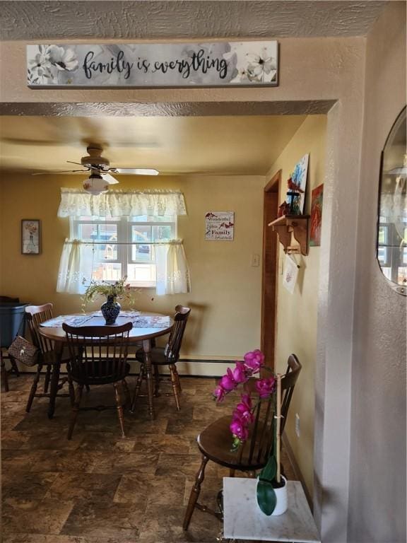 dining area featuring a baseboard heating unit, stone finish flooring, arched walkways, baseboards, and ceiling fan