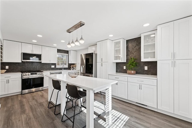 kitchen with light countertops, white cabinets, glass insert cabinets, appliances with stainless steel finishes, and a kitchen bar