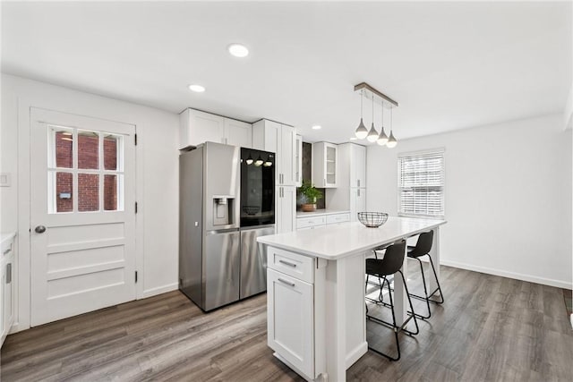 kitchen featuring dark wood-type flooring, a breakfast bar, stainless steel refrigerator with ice dispenser, white cabinetry, and light countertops