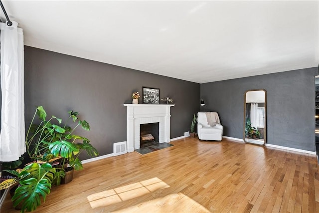 unfurnished living room featuring visible vents, wood finished floors, arched walkways, baseboards, and a brick fireplace