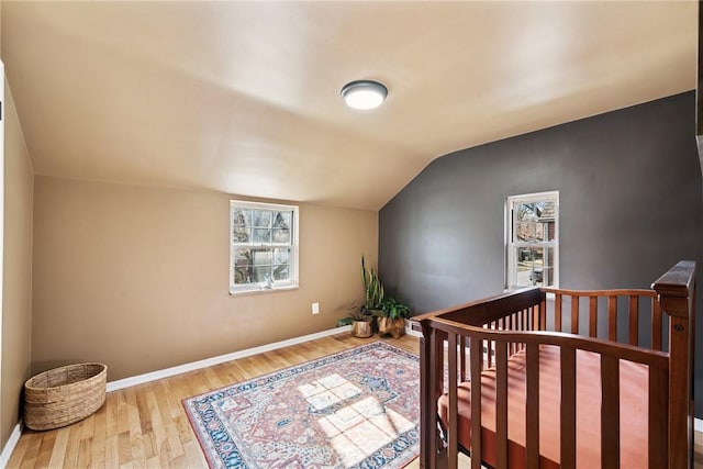 bedroom with vaulted ceiling, a nursery area, wood finished floors, and baseboards