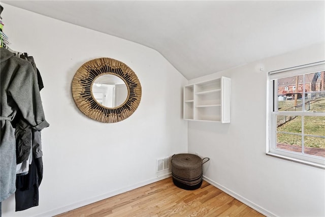 interior space featuring visible vents, baseboards, vaulted ceiling, and light wood finished floors