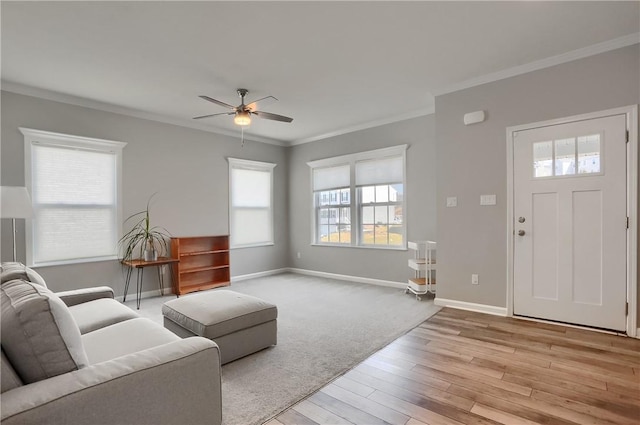 living area with light wood-type flooring, baseboards, ornamental molding, and a ceiling fan