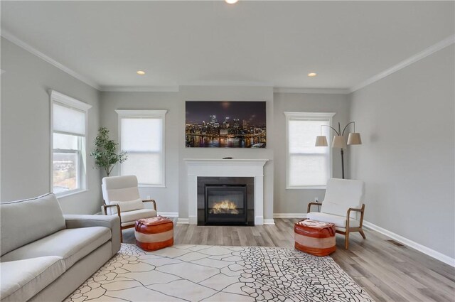 living room with wood finished floors, baseboards, recessed lighting, ornamental molding, and a glass covered fireplace