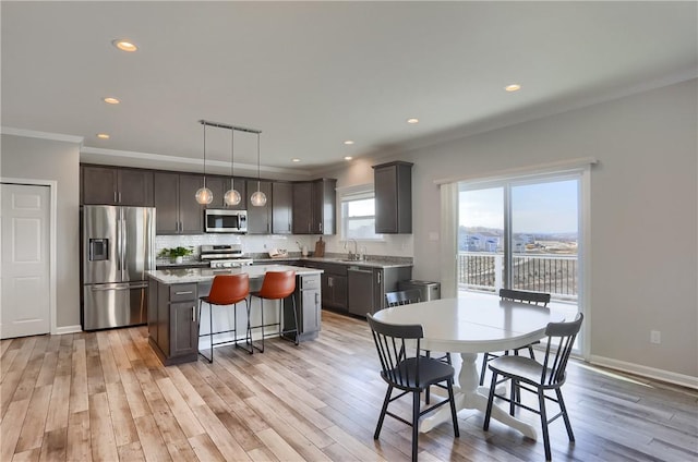 kitchen featuring ornamental molding, light wood-style floors, appliances with stainless steel finishes, backsplash, and a center island