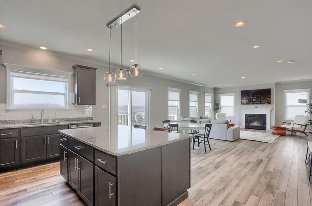 kitchen featuring light wood finished floors, recessed lighting, a sink, a glass covered fireplace, and crown molding