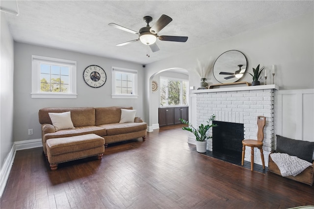 living room with a ceiling fan, hardwood / wood-style flooring, a textured ceiling, baseboards, and a brick fireplace