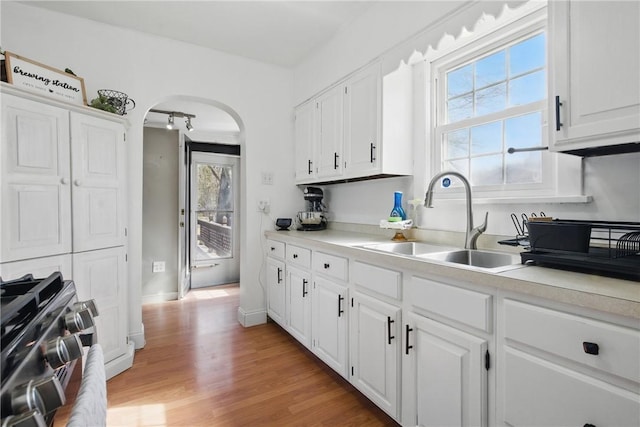 kitchen featuring arched walkways, light wood finished floors, light countertops, and a sink