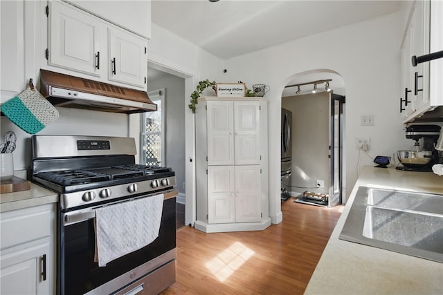 kitchen with stainless steel gas range oven, light wood finished floors, under cabinet range hood, arched walkways, and light countertops