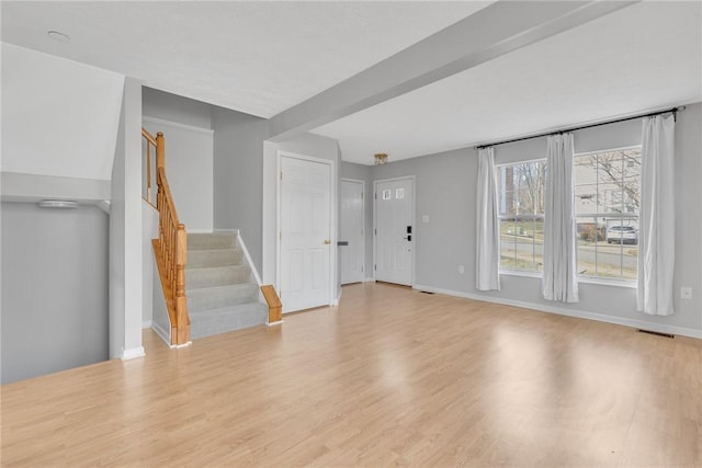 unfurnished living room featuring stairway, visible vents, baseboards, and wood finished floors