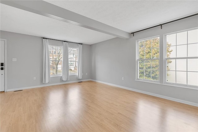 unfurnished living room featuring beamed ceiling, baseboards, light wood finished floors, and a textured ceiling