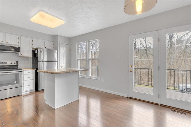 kitchen with visible vents, wood finished floors, white cabinetry, stainless steel appliances, and baseboards