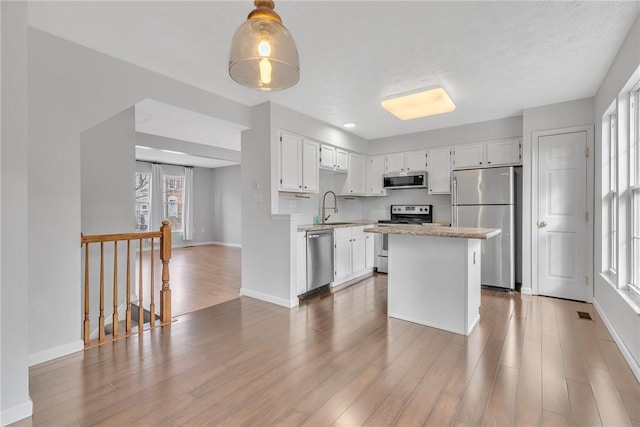 kitchen with a wealth of natural light, appliances with stainless steel finishes, wood finished floors, and a center island