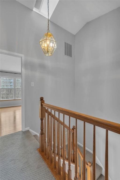 stairway with a chandelier, visible vents, baseboards, and lofted ceiling