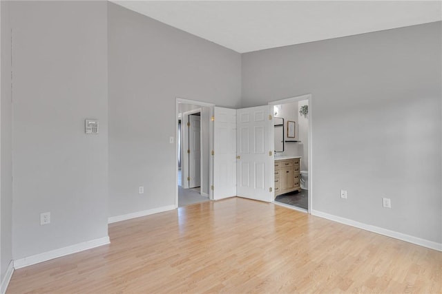 interior space with baseboards, light wood-style flooring, and a towering ceiling