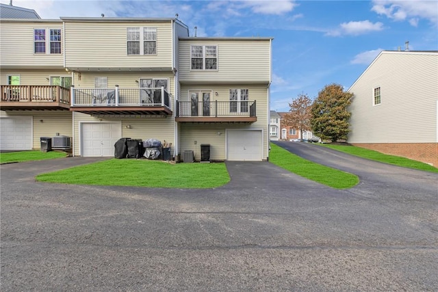 rear view of property featuring aphalt driveway, a lawn, central AC unit, and an attached garage