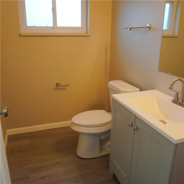 half bathroom with a wealth of natural light, toilet, wood finished floors, and vanity