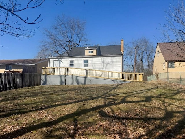 rear view of property featuring a chimney, a lawn, a wooden deck, and fence