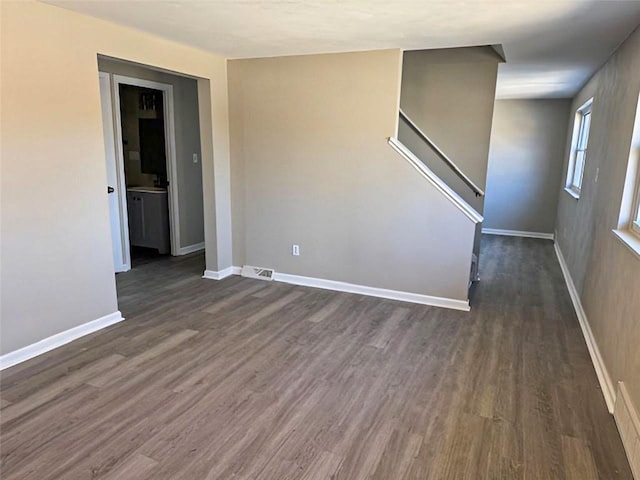 empty room featuring stairway, dark wood-style floors, visible vents, and baseboards