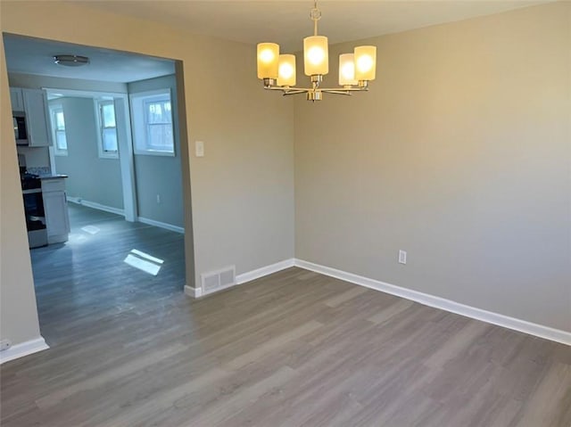 spare room featuring visible vents, an inviting chandelier, dark wood-type flooring, and baseboards