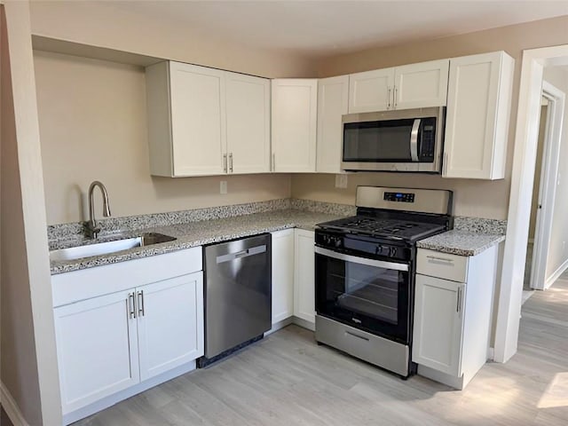 kitchen with light wood-type flooring, light stone counters, white cabinets, stainless steel appliances, and a sink