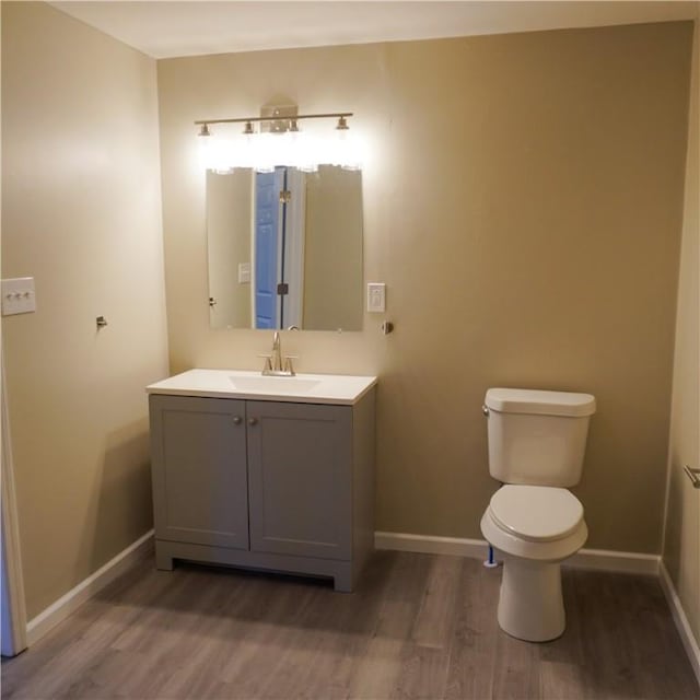 bathroom featuring baseboards, toilet, wood finished floors, and vanity