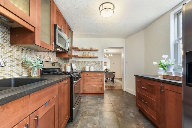 kitchen featuring dark countertops, a sink, decorative backsplash, appliances with stainless steel finishes, and open shelves