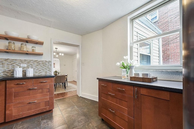 kitchen with open shelves, backsplash, dark countertops, a textured ceiling, and baseboards