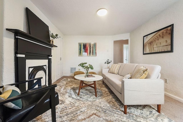 living area featuring visible vents, a textured ceiling, a fireplace, baseboards, and a textured wall