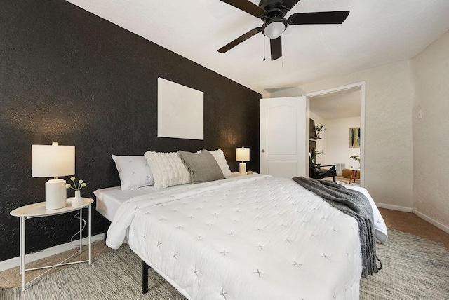 carpeted bedroom with a ceiling fan, an accent wall, and baseboards