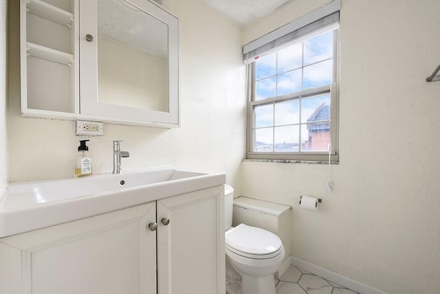 bathroom featuring vanity, toilet, a textured wall, and baseboards