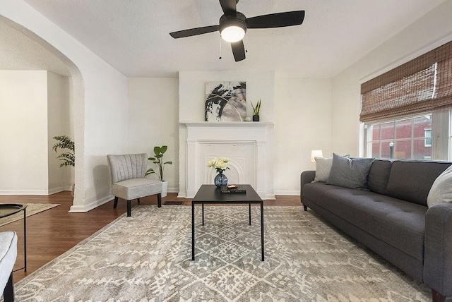 living area with arched walkways, a fireplace, baseboards, and wood finished floors