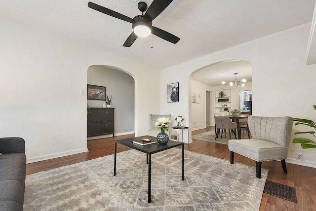 living room featuring arched walkways, visible vents, baseboards, and wood finished floors