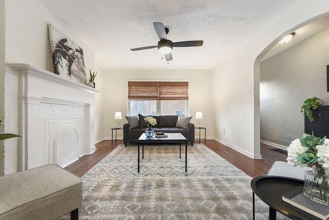 living room featuring baseboards, arched walkways, a textured ceiling, and wood finished floors