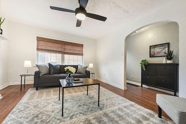 living room featuring baseboards, arched walkways, a textured ceiling, and wood finished floors