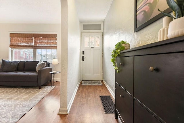 foyer featuring wood finished floors, a textured wall, baseboards, and visible vents